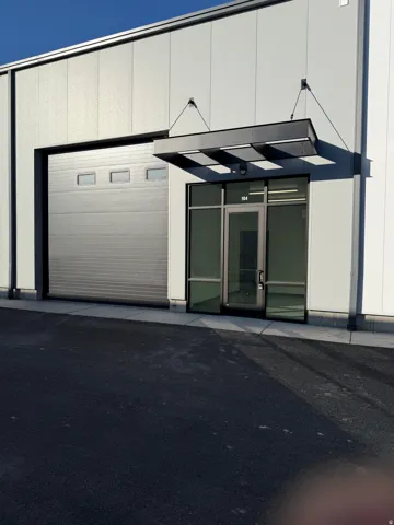 Modern commercial exterior with a prominent roll-up door, glass entry door, overhead awning, and paved lot