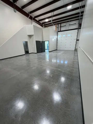 Polished concrete flooring, high ceilings with exposed structural beams, multiple interior doors, and a large roll-up door with integrated windows