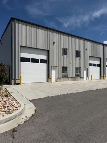 Metal-sided commercial building featuring multiple roll-up doors with window panels, individual entry doors, and concrete driveways