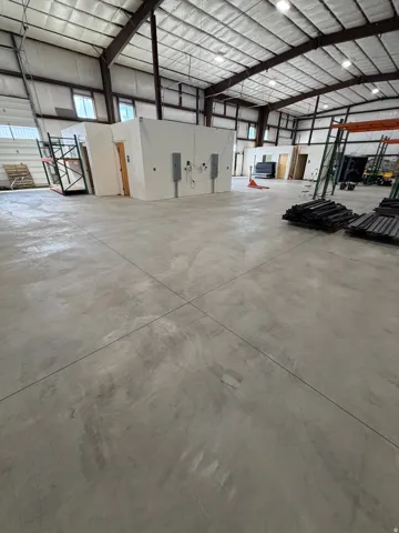 Spacious open interior with a concrete floor, exposed structural beams, insulated ceiling, and multiple windows