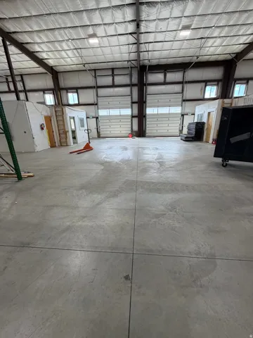 Expansive concrete flooring with two large overhead doors and multiple high-set windows