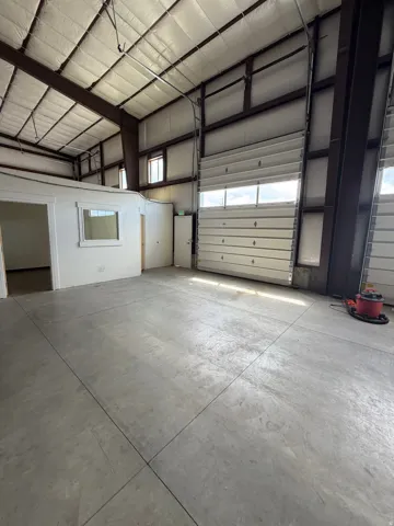 Open interior space with exposed structural beams, a roll-up door, and concrete flooring