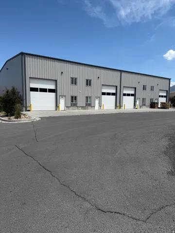 Metal-sided commercial building featuring multiple roll-up doors, individual entry doors, and ground-level windows