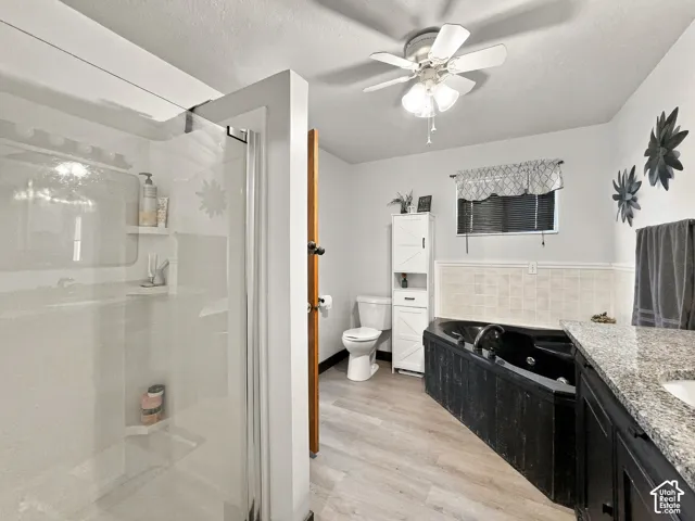 Glass-enclosed shower, built-in soaking tub, wood-finish flooring, granite-look countertop, and ceiling fan with integrated lighting
