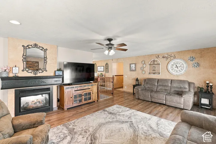 Living room featuring a fireplace with a black mantel, wood-finish flooring, and a ceiling fan