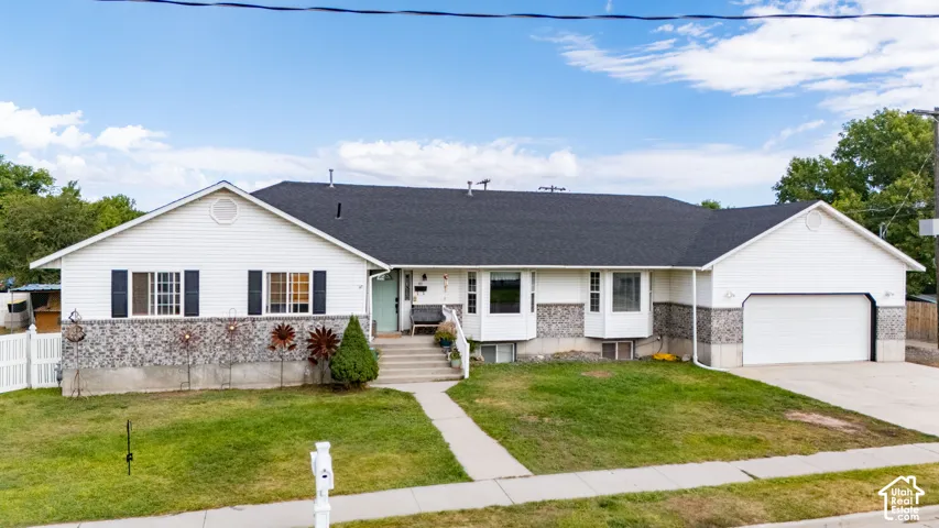 White siding exterior with stone accent, black shingle roof, attached garage with white door, and a concrete driveway