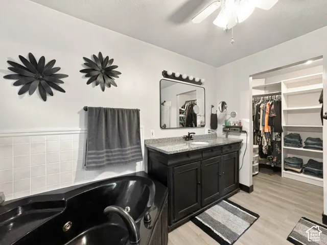 Bathroom featuring a built-in black jetted tub, a vanity with a granite countertop, wood-finish flooring, and an organized walk-in closet with built-in shelving