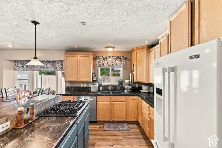 Kitchen featuring wood-finish flooring, a built-in gas range on an island, wood cabinetry, dark countertops, and a stainless steel dishwasher