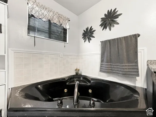 Corner bathtub with a dark finish, integrated faucet, and surrounding tile wainscoting