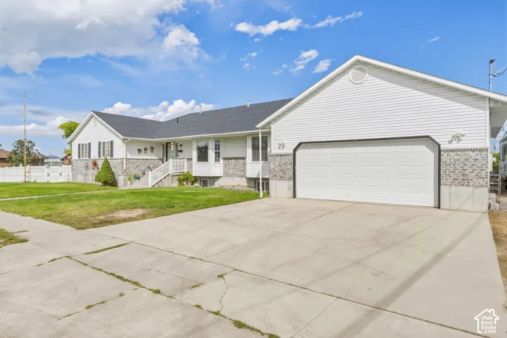 White siding exterior with a dark shingle roof, stone accents, attached garage with white door, and a concrete driveway