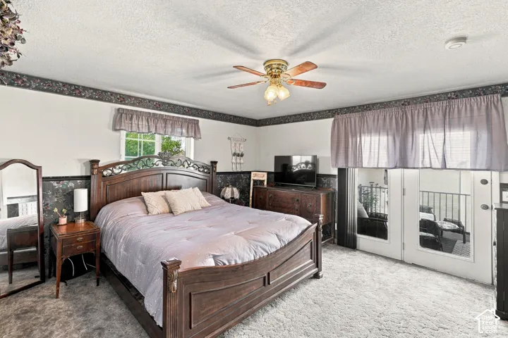 Carpeted room featuring a ceiling fan with integrated lighting, a window, and double doors opening to an outdoor area