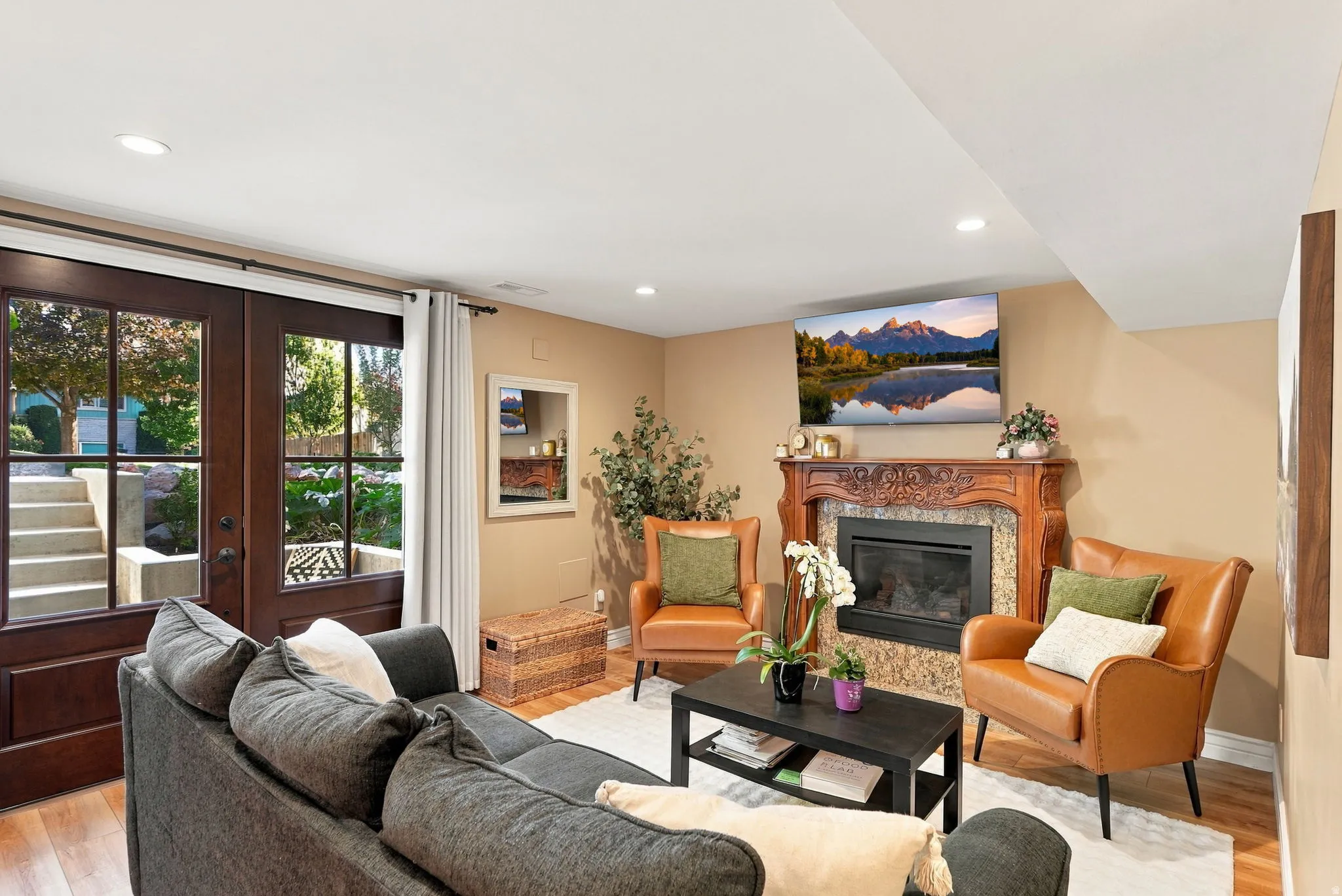 Warm living space featuring rich wood-finish flooring, recessed lighting, and a stone-clad fireplace with an ornate mantel