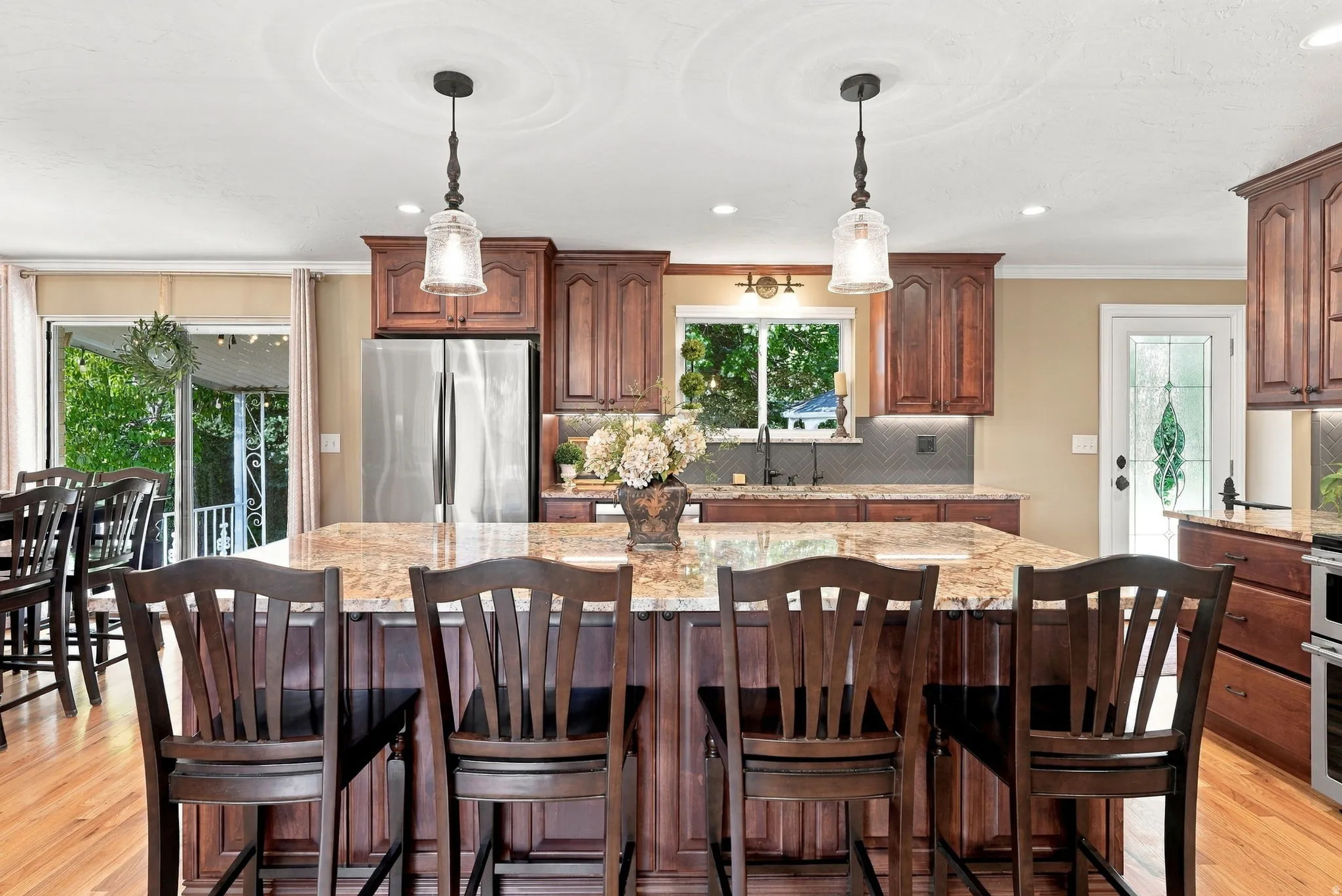 Kitchen featuring a central island with a stone countertop, stained wood cabinetry, stainless steel refrigerator, hardwood flooring, and pendant lighting