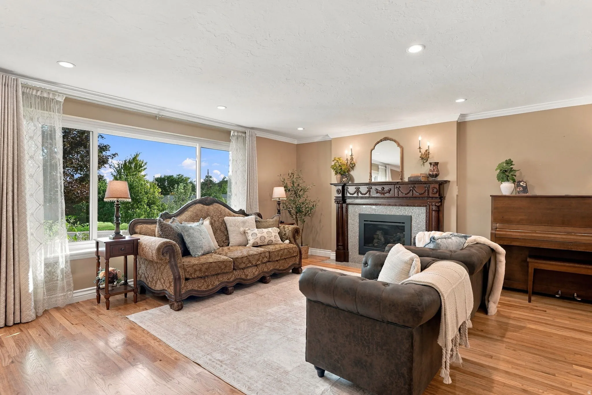 Recessed lighting, crown molding, wood-finish flooring, a decorative fireplace with a mantel, and expansive windows