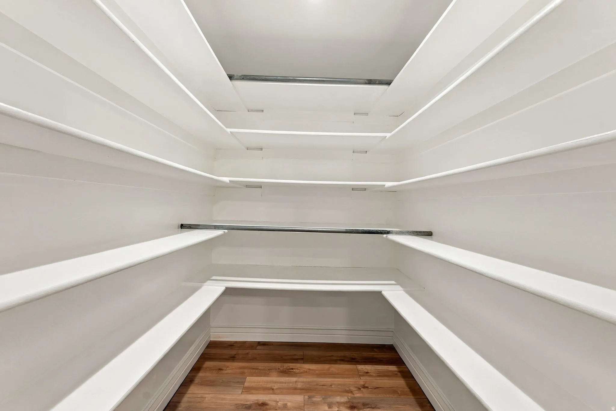 Expansive storage space featuring built-in shelving, wood-finish flooring, and a dedicated hanging rod