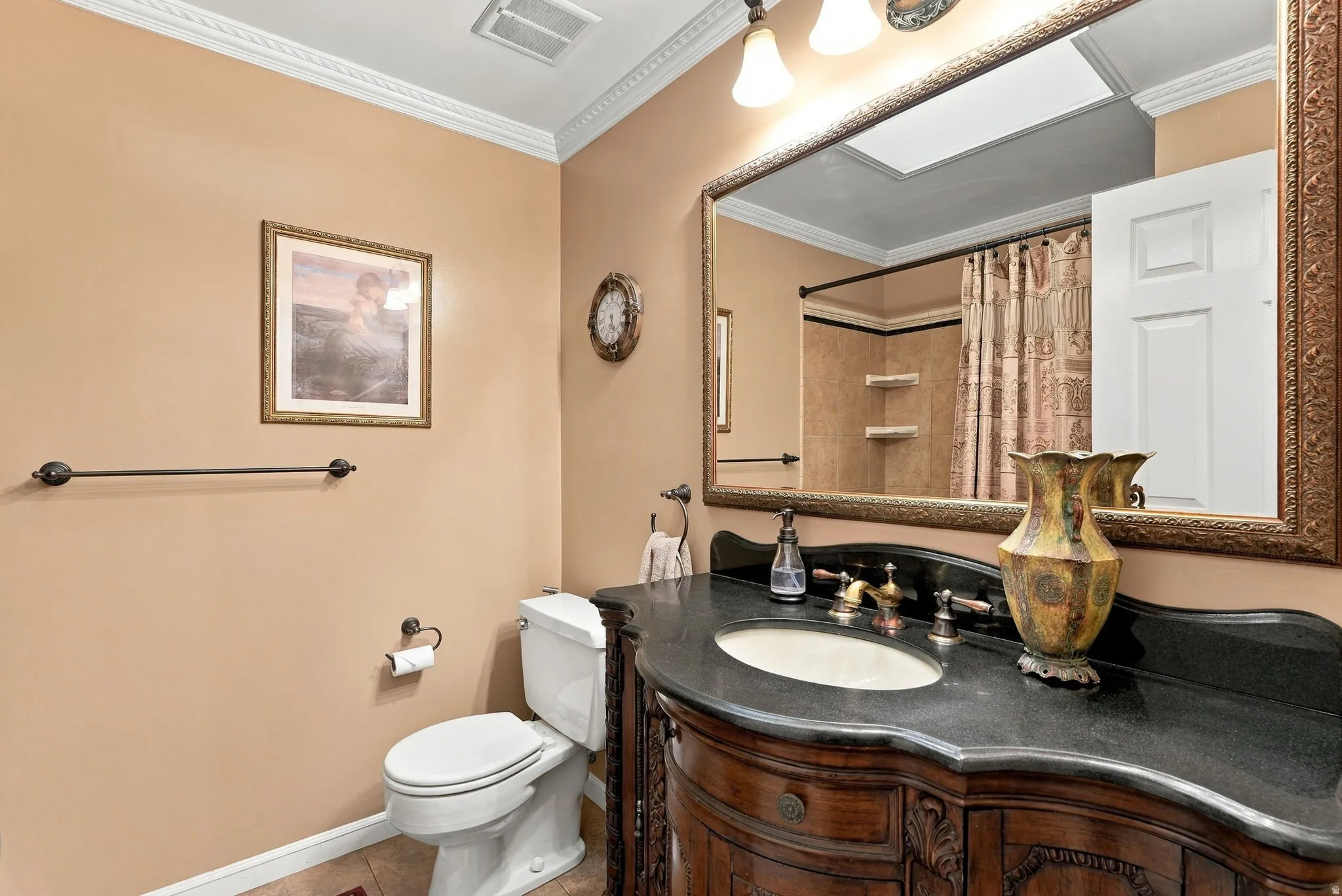 Bathroom featuring an ornate wood vanity with an undermount sink, dark countertop, and a framed mirror with integrated lighting