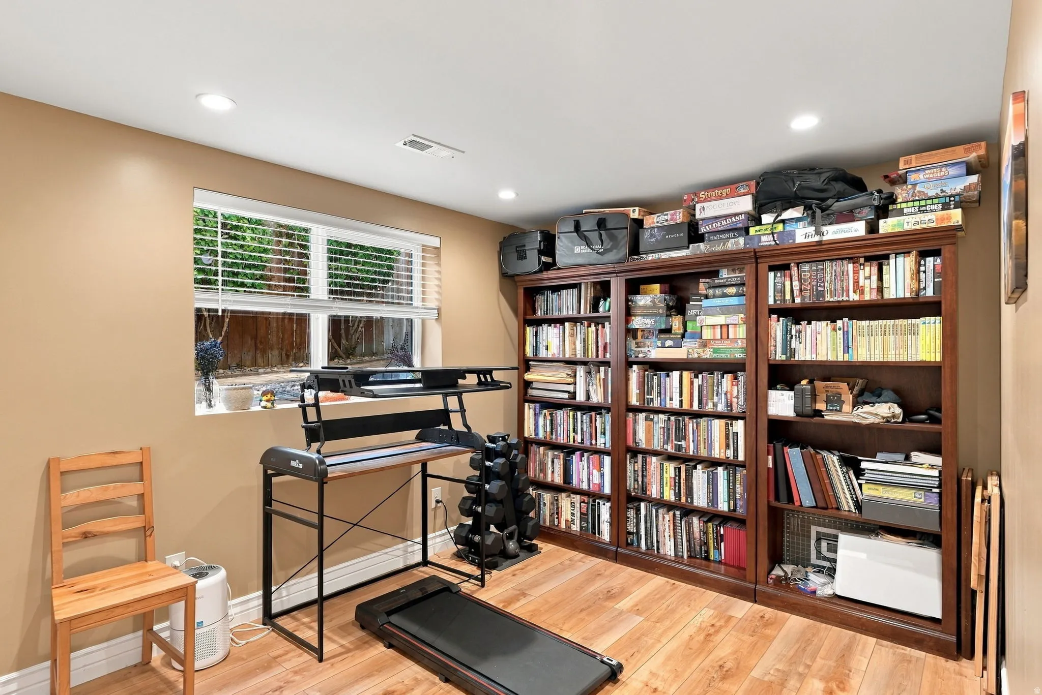 Wood-finish flooring, built-in shelving units, recessed lighting, and a window with blinds