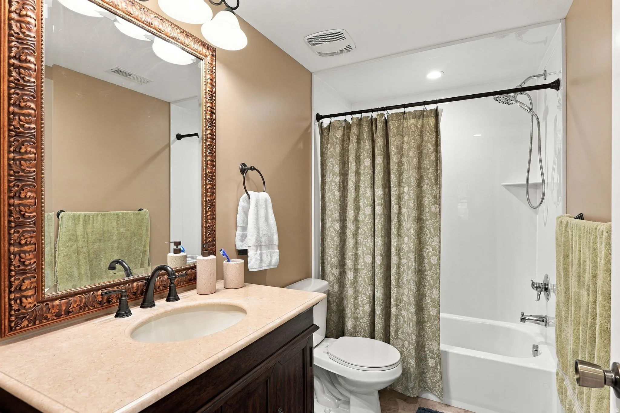 Bathroom featuring a vanity with an integrated sink, dark wood-finish cabinetry, a large framed mirror, and an adjacent shower-over-tub combination with a wall-mounted shower head