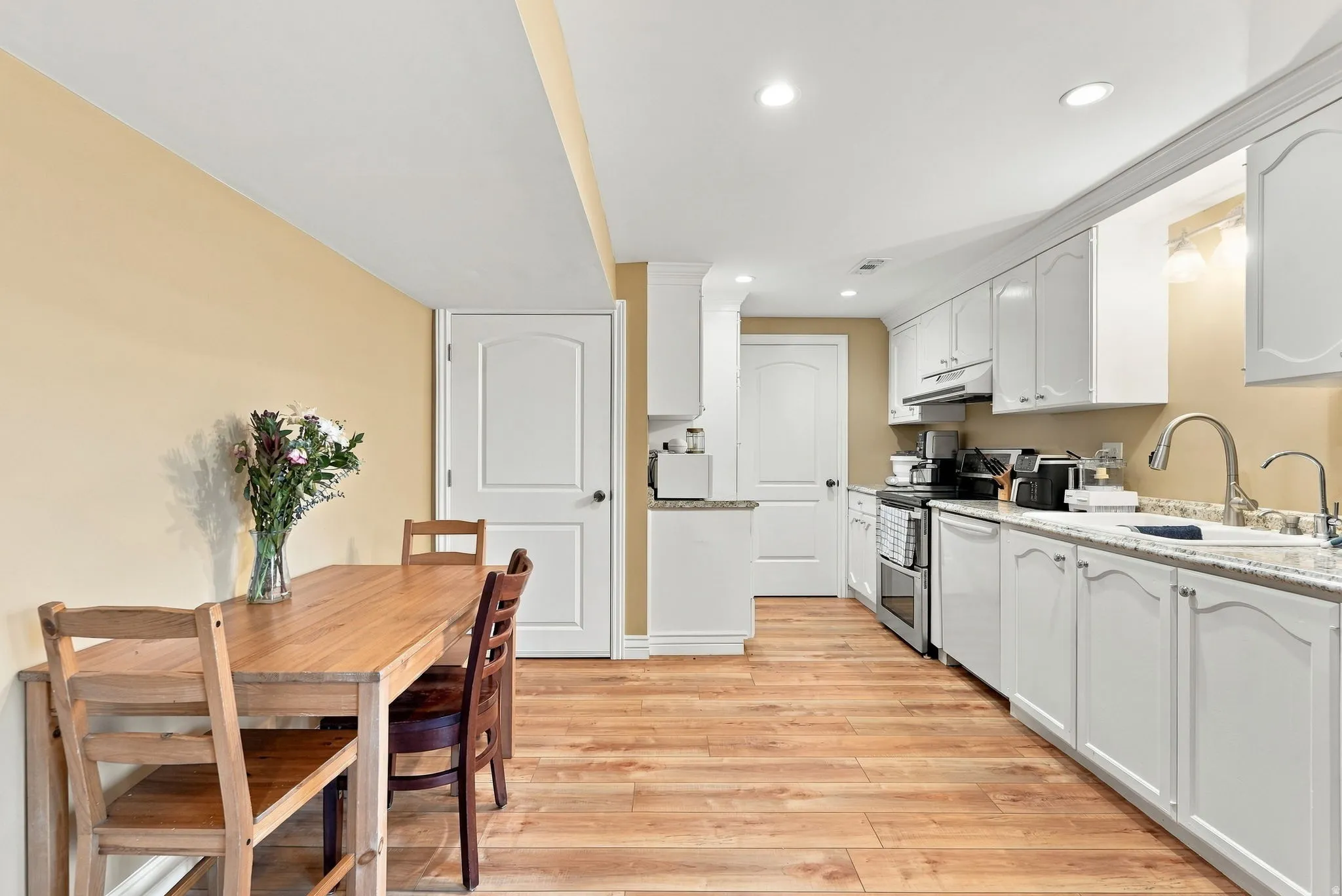 Wood-finish flooring throughout, white cabinetry with crown molding, stainless steel kitchen appliances, and recessed ceiling lighting