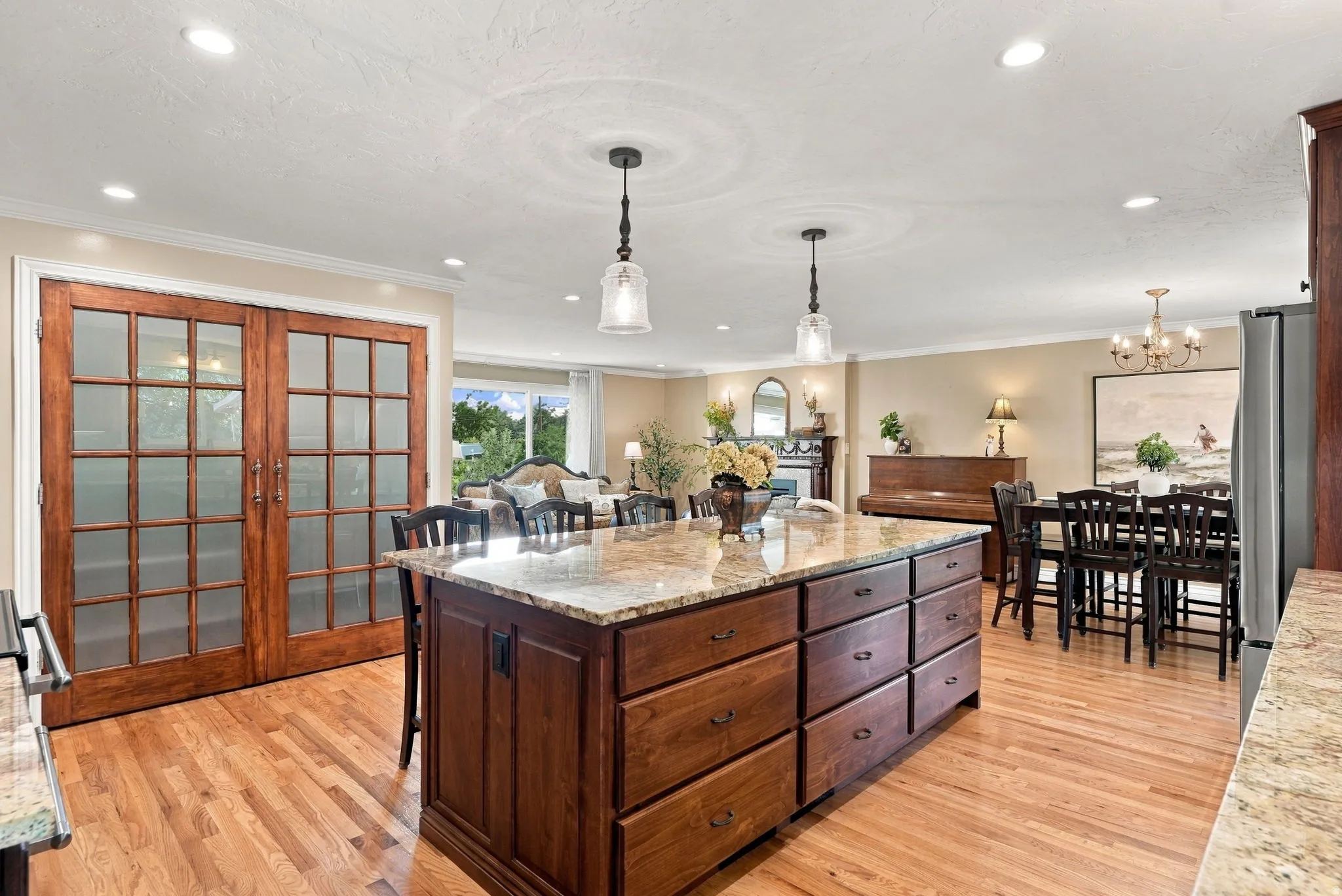 Expansive kitchen island with granite countertop, wood-finish flooring, recessed lighting, and elegant pendant lighting
