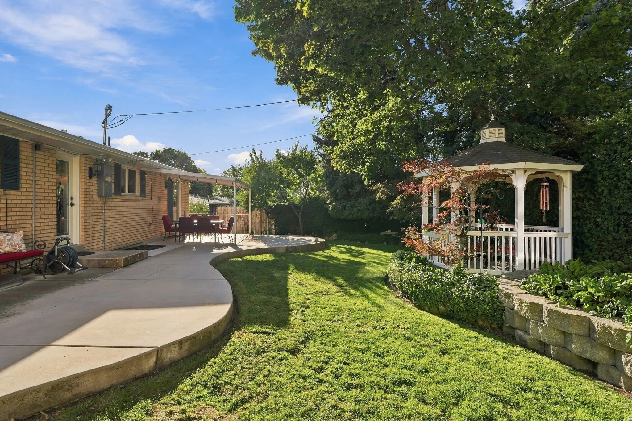 Brick exterior, covered patio, curved concrete pathway, white gazebo, terraced landscaping