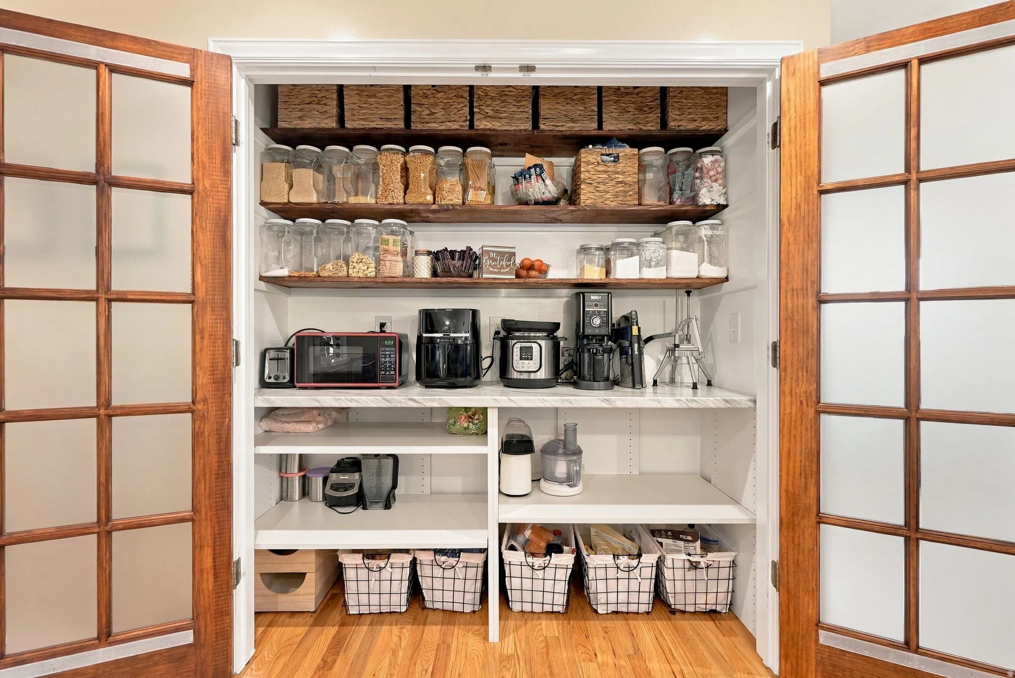 Custom pantry with wood-finish shelving and white cabinetry, featuring a countertop workspace and hardwood flooring