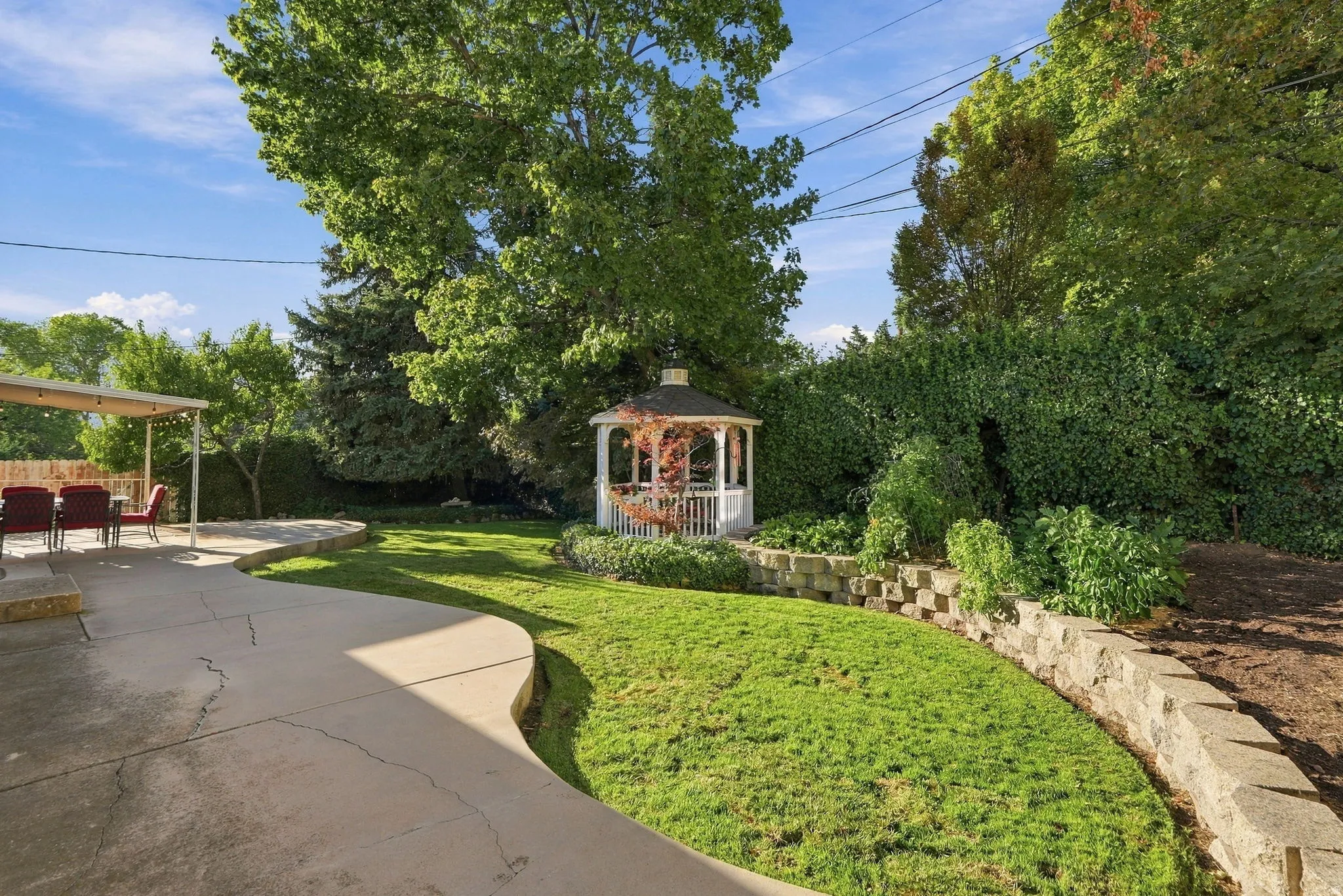 Expansive backyard featuring a gazebo, concrete patio, and tiered stone retaining walls