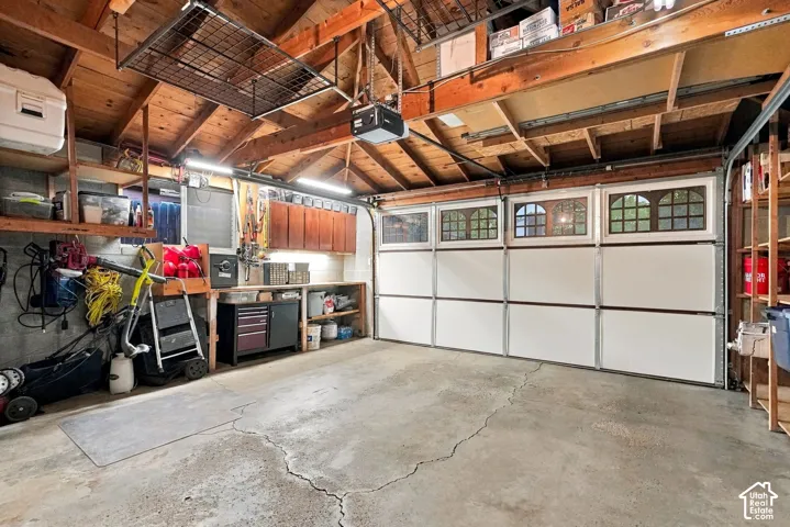 Concrete flooring garage with an exposed wood beam ceiling, suspended overhead storage, and built-in wall shelving