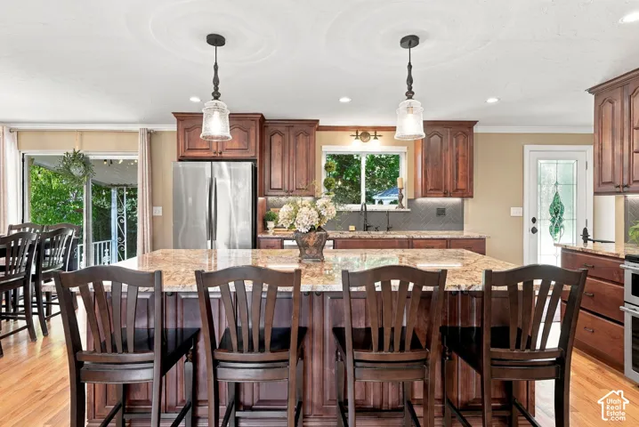 Kitchen featuring a central island with a stone countertop, stained wood cabinetry, stainless steel refrigerator, hardwood flooring, and pendant lighting