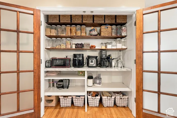 Custom pantry with wood-finish shelving and white cabinetry, featuring a countertop workspace and hardwood flooring