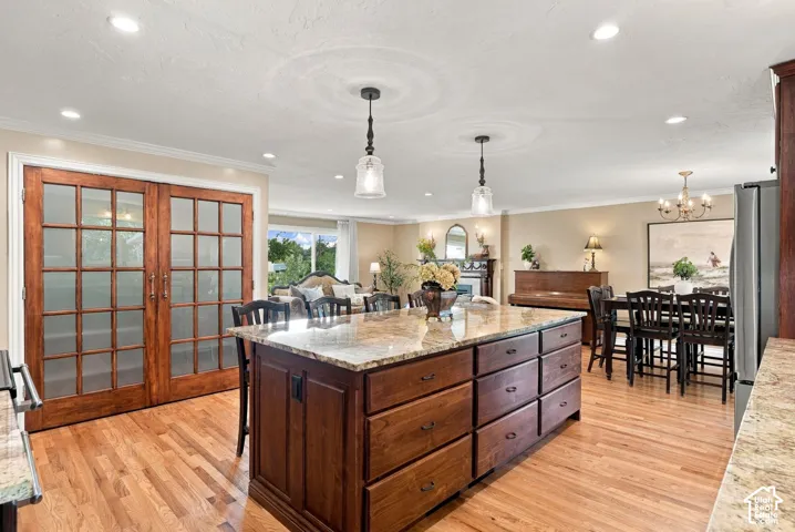 Expansive kitchen island with granite countertop, wood-finish flooring, recessed lighting, and elegant pendant lighting
