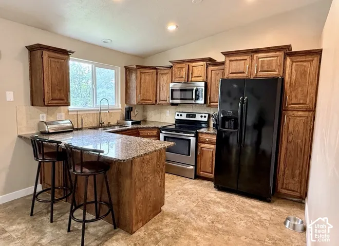 Kitchen featuring wood cabinetry, granite countertops, stainless steel appliances, a tiled backsplash, and an eat-at peninsula