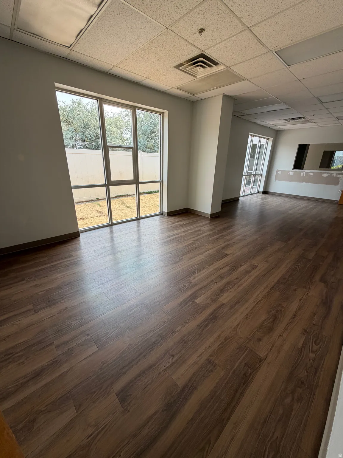 Wood-finish flooring, drop ceiling with integrated lighting, and multiple large windows with exterior access