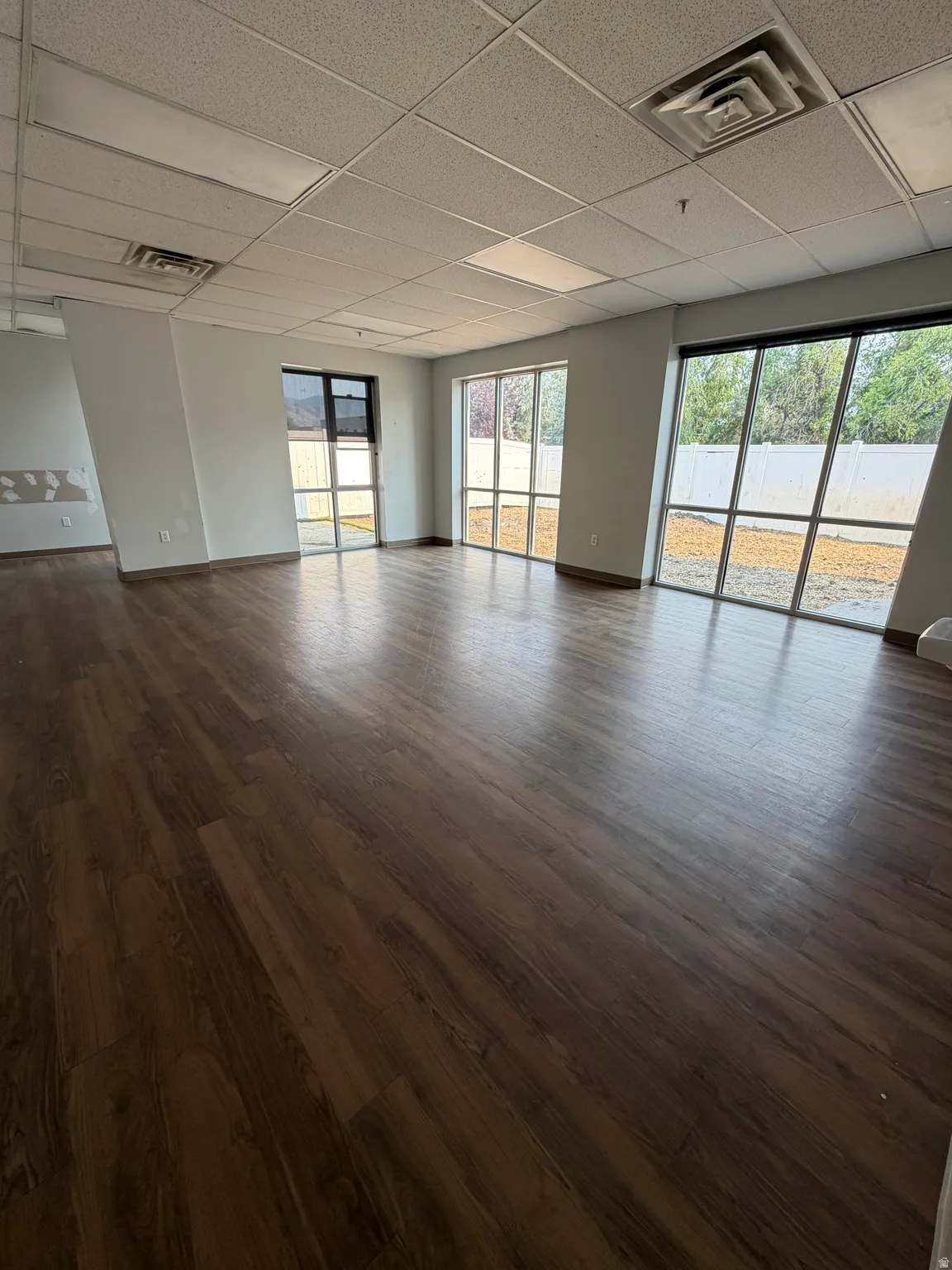Expansive room featuring wood-finish flooring, multiple large windows, and a dropped ceiling with recessed lighting