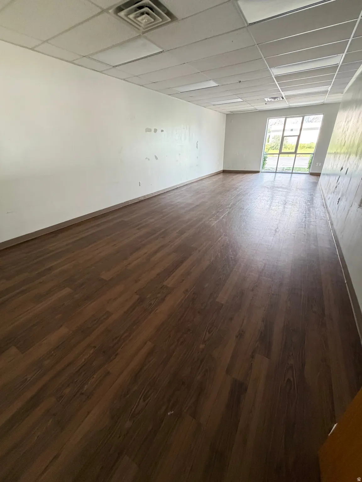 Expansive room featuring wood-finish flooring and a drop ceiling with recessed lighting