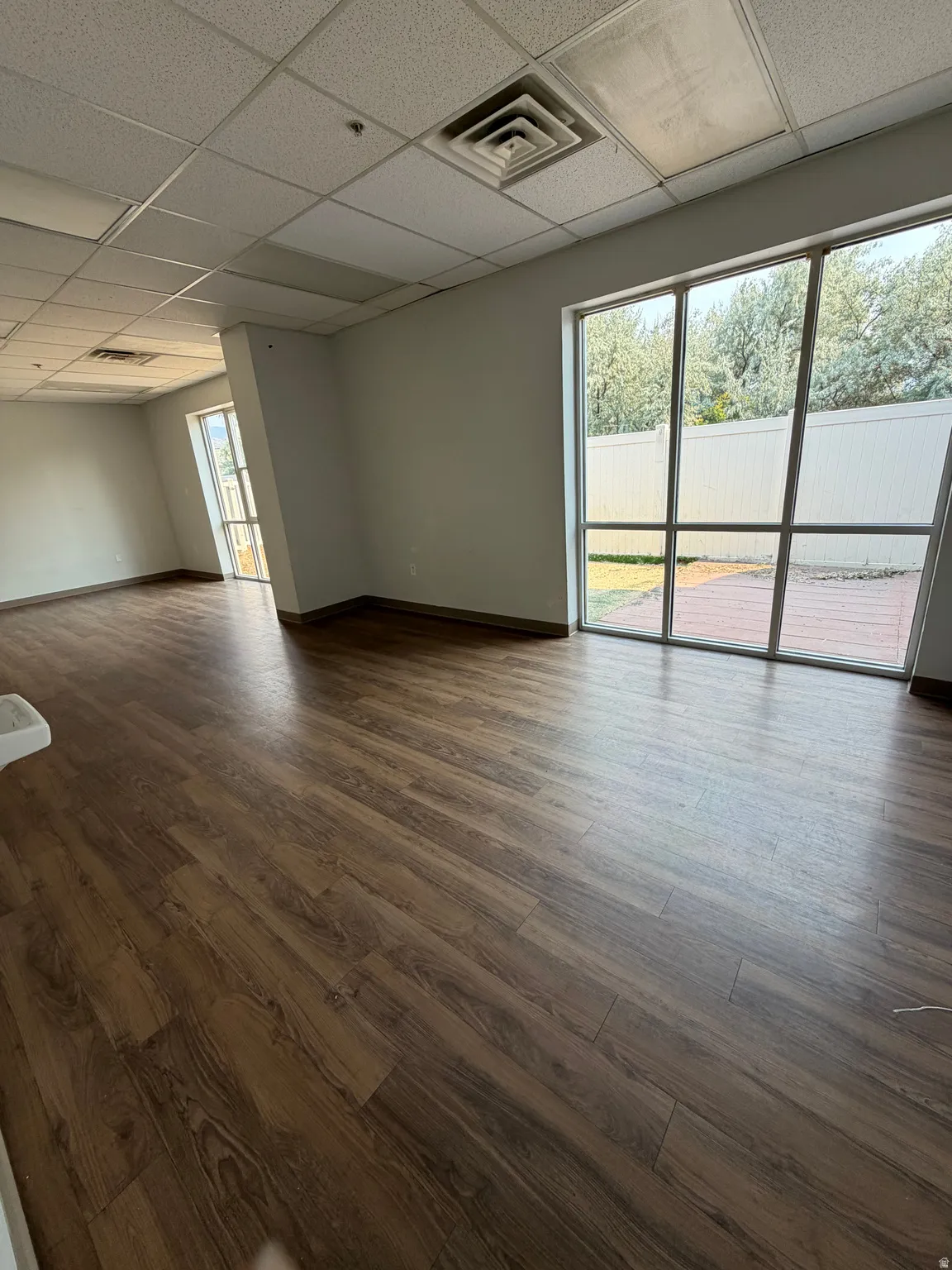 Expansive room featuring wood-finish flooring, drop ceiling, and large windows