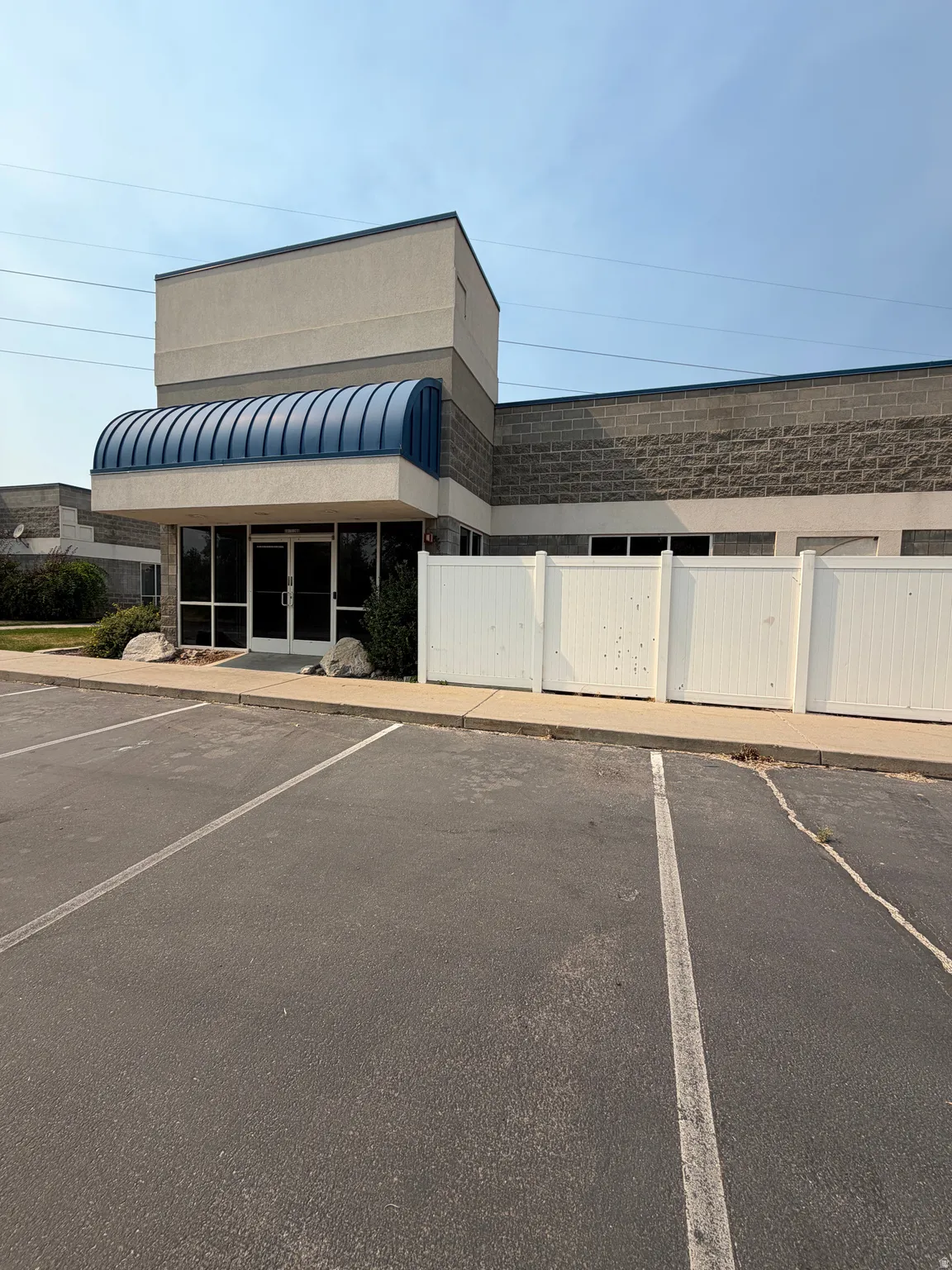 Building exterior with a blue curved awning, full-light entry doors, and a parking area with painted stalls