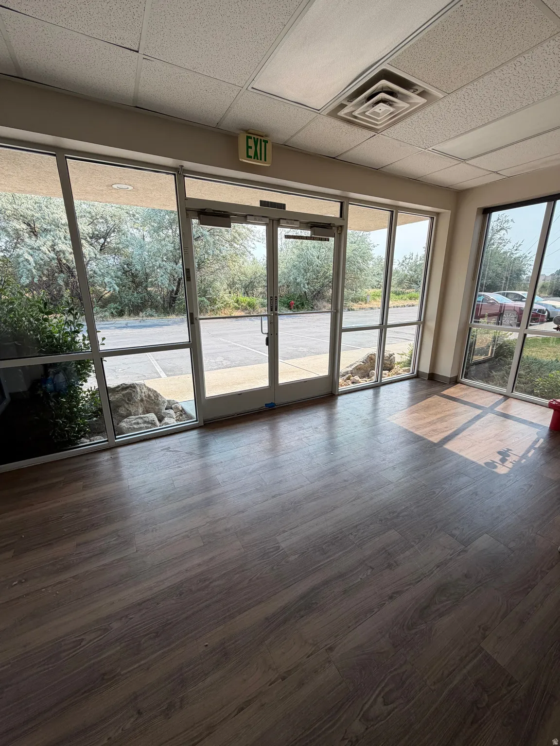 Wide plank wood-finish flooring, full-light entry doors, expansive window panels, suspended ceiling with integrated lighting