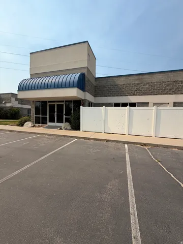 Building exterior with a blue curved awning, full-light entry doors, and a parking area with painted stalls