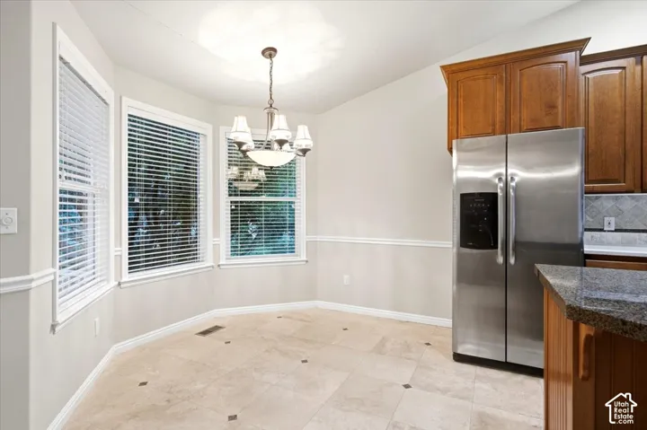 Bay window with white blinds, neutral tiled flooring with dark accent tiles, stainless steel refrigerator, and wood cabinetry
