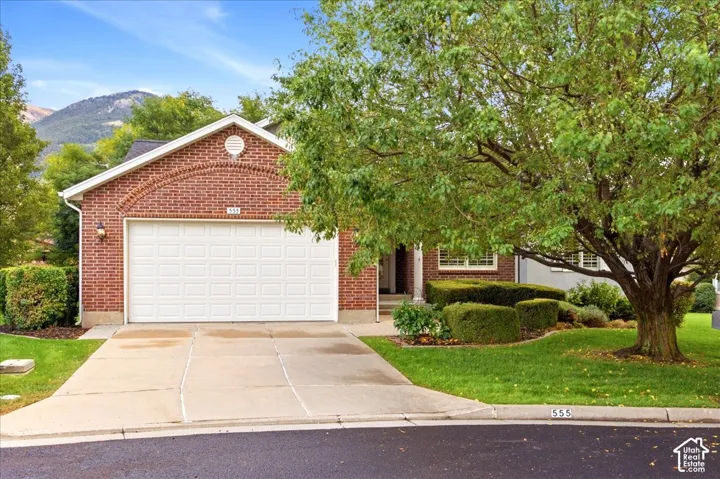 Brick exterior with a prominent arched detail, white garage door, concrete driveway, and established front yard landscaping with mature trees