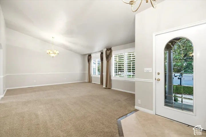 Vaulted ceiling, two chandeliers, wainscoting, plantation shutters, and a front entry door with an arched glass insert