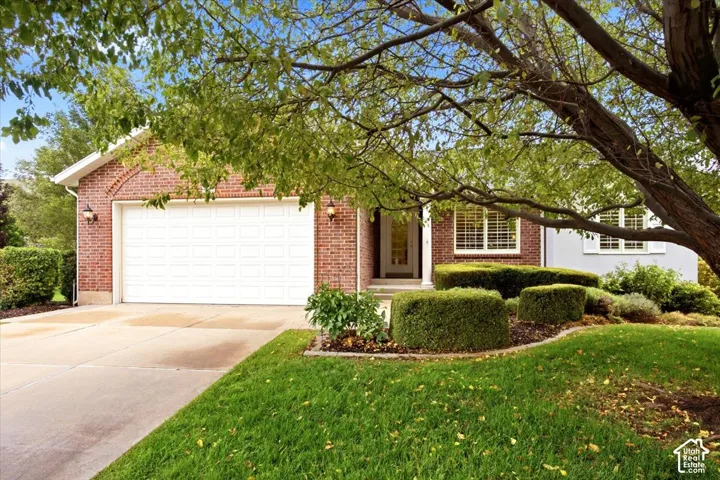 Brick exterior with a white garage door, concrete driveway, and established landscaping with mature trees