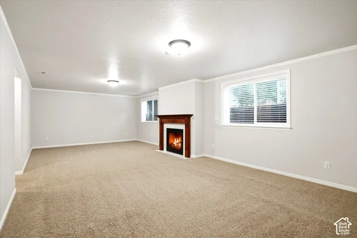 Spacious room with a built-in fireplace featuring a wood surround, light beige carpeting, multiple windows with blinds, and recessed ceiling lighting