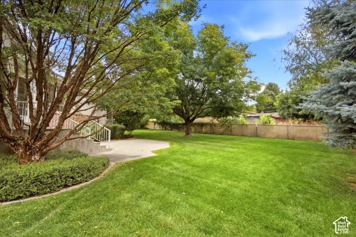 Expansive green lawn, mature trees, concrete patio, concrete retaining wall, and metal handrails