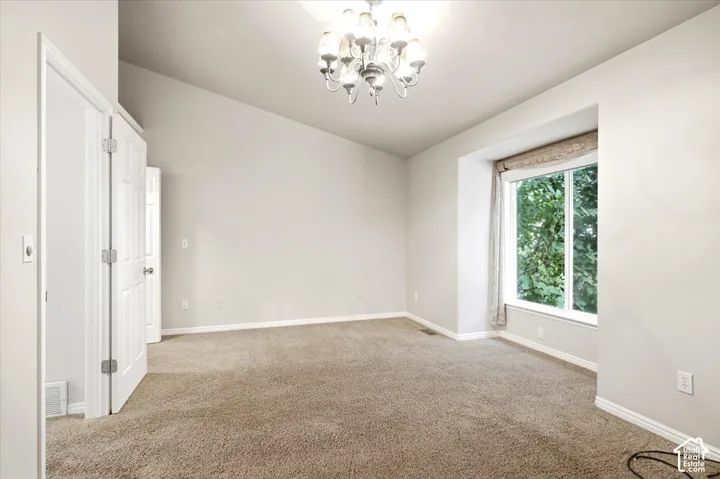 Vaulted ceiling with chandelier, neutral carpeting, window with recessed framing, and white paneled doors