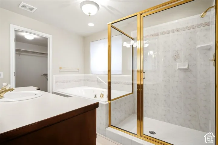 Enclosed shower with gold-tone frame, white tiled walls, built-in bathtub, vanity with integrated sink, and an open closet