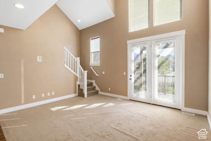 Vaulted ceiling with recessed lighting, double glass doors, upper transom windows, and a carpeted staircase with white railings