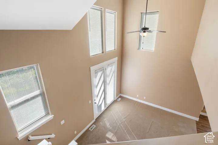 Vaulted ceiling with a ceiling fan, multiple windows, French doors, and carpeted flooring