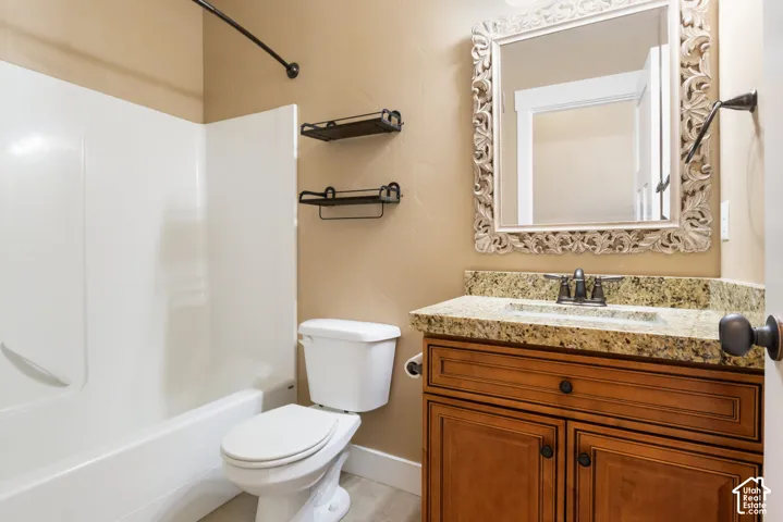 White tub and shower combination, wood-finish vanity with a granite countertop, undermount sink, and a framed mirror